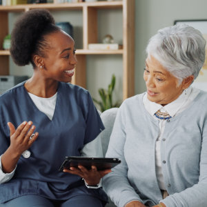 nurse happily explaining something from the tablet to senior woman